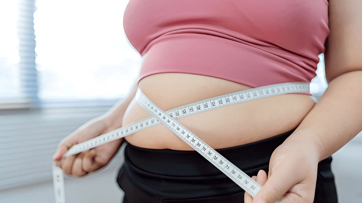 A person measuring their waist with a tape, symbolizing the importance of monitoring weight to prevent obesity and associated health risks.