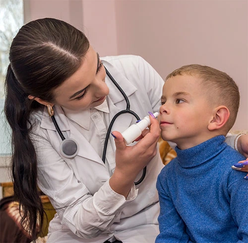 Doctor examining a young boy with a medical device, providing care for childhood asthma in a clinical setting.